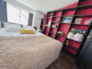 Une chambre d’hôtel avec un grand lit, une bibliothèque rouge et noire et une fenêtre avec des rideaux.
