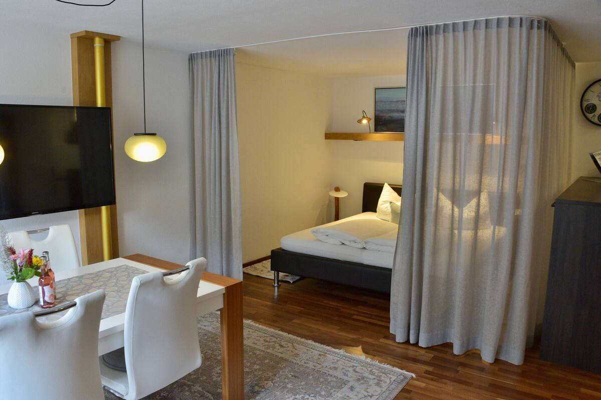 Una habitación de hotel con cama, televisión, mesa de comedor con sillas y un escritorio pequeño.