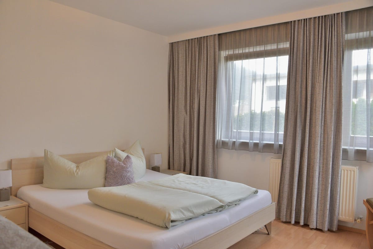 A hotel room with a bed, a nightstand, a lamp, and a window with curtains.
