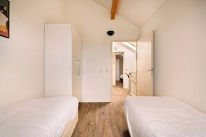 Une chambre avec deux lits, une armoire et une porte donnant sur une autre pièce.