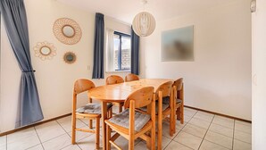 A dining area with a round wooden table, six chairs, and a hanging light fixture. - Villa in Julianadorp Near Sandy Beach (Julianadorp)