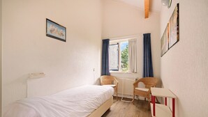 A small, well-lit room with a single bed, two wicker chairs, a radiator, and a window with curtains. - Villa in Julianadorp Near Sandy Beach (Julianadorp)