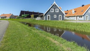 A canal with houses on one side and a modern building with a sloped roof on the other. - Villa in Julianadorp Near Sandy Beach (Julianadorp)