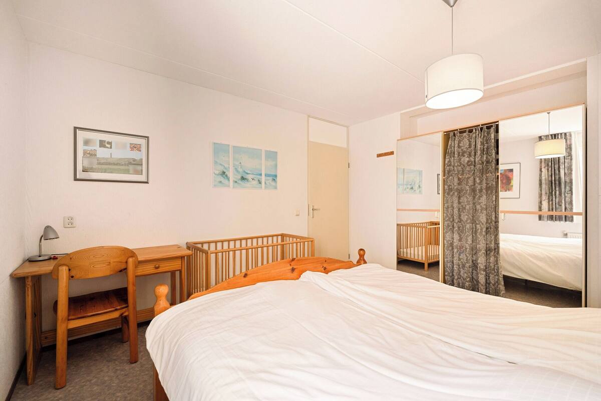 A bedroom with a bed, a desk, a chair, and a mirror.