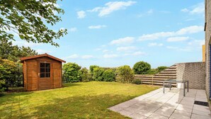 A wooden shed, a patio with a table and chairs, and a brick wall. - Villa in Julianadorp Near Sandy Beach (Julianadorp)