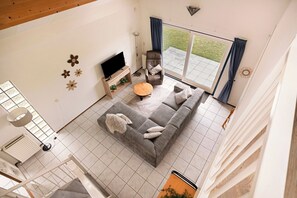 Un salon moderne avec un canapé gris, un téléviseur et une grande fenêtre avec des rideaux.