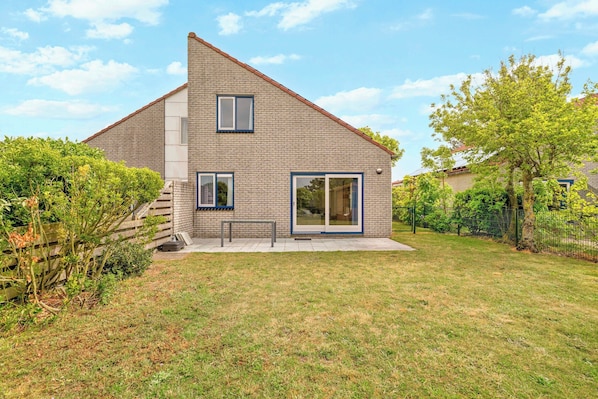 Une maison à deux étages, avec une façade en briques, un porche à l’avant et une grande porte-fenêtre coulissante.