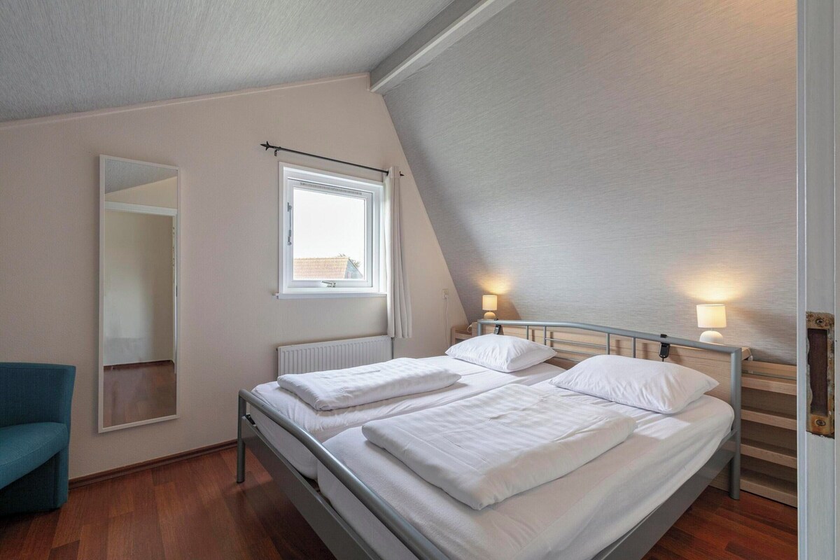 A bedroom with two beds, a window, a mirror, and a chair.
