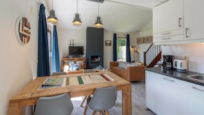 A cozy living room with a fireplace, a dining area with a wooden table, and a kitchen with white cabinets and a coffee maker. - Yperhof 66 Holiday Home for 6 Guests on Cost (Julianadorp)