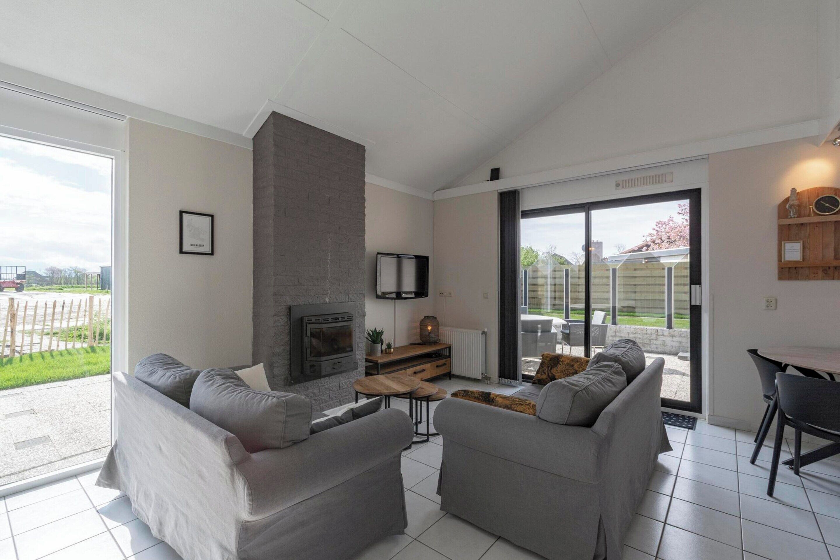 A modern living room with two grey sofas, a fireplace, a TV, and a dining area with a table and chairs.