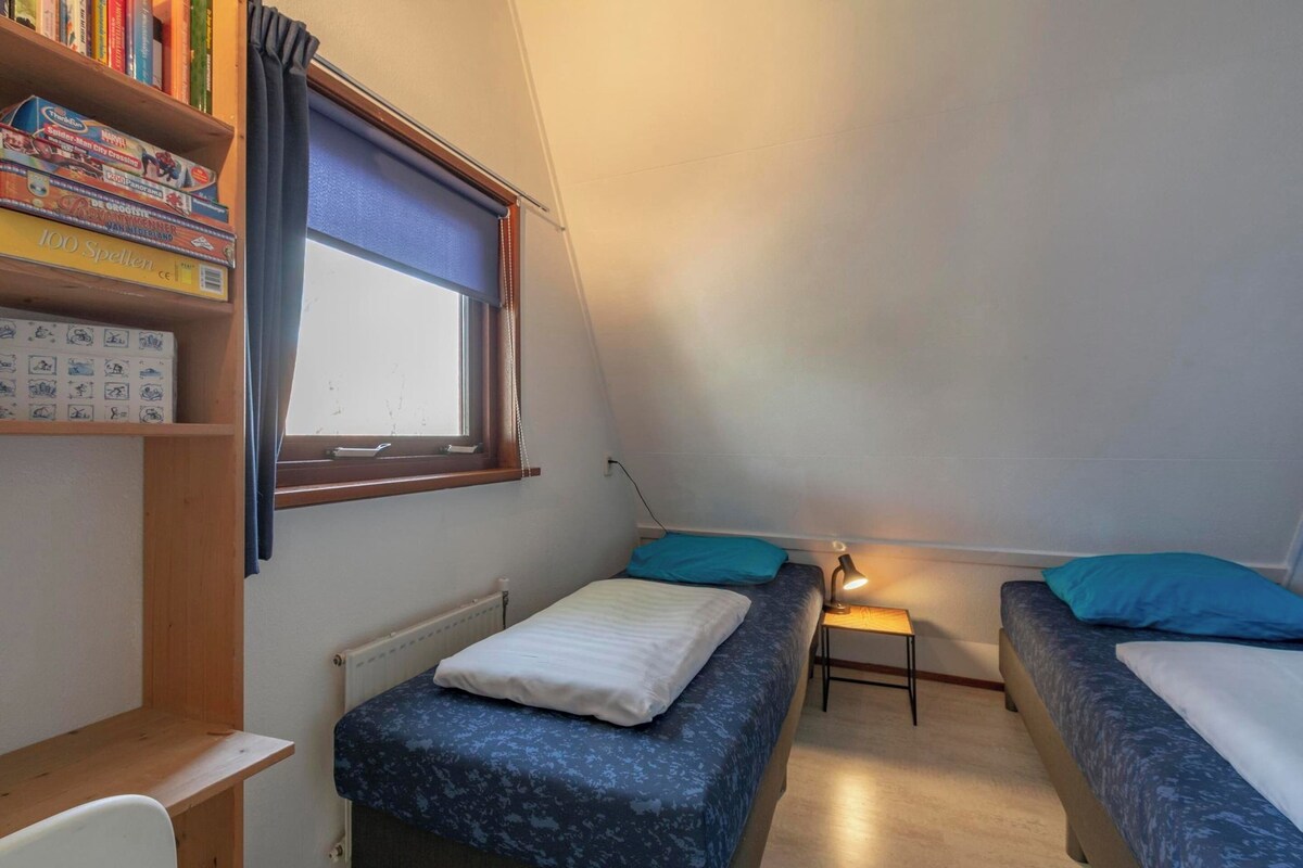 A dormitory room with two beds, a desk, a bookshelf, and a window with curtains.