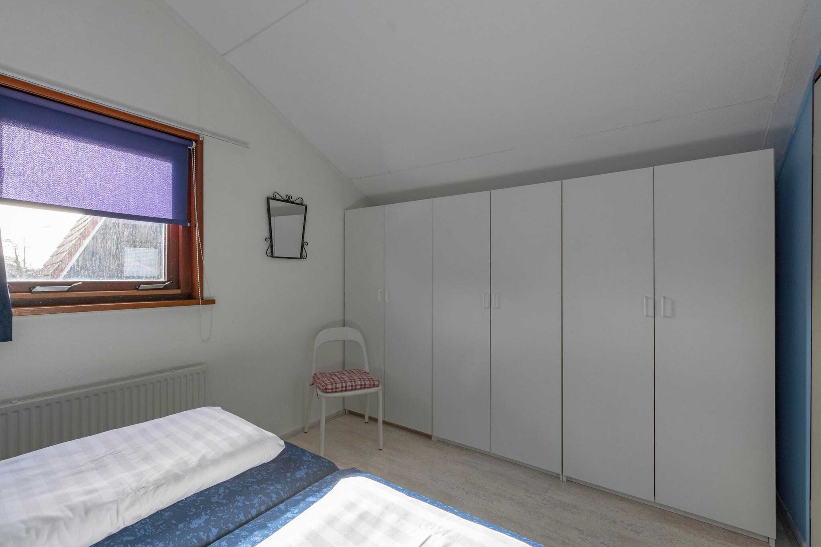 Een slaapkamer met een bed, een stoel, een kledingkast en een raam met een gordijn.