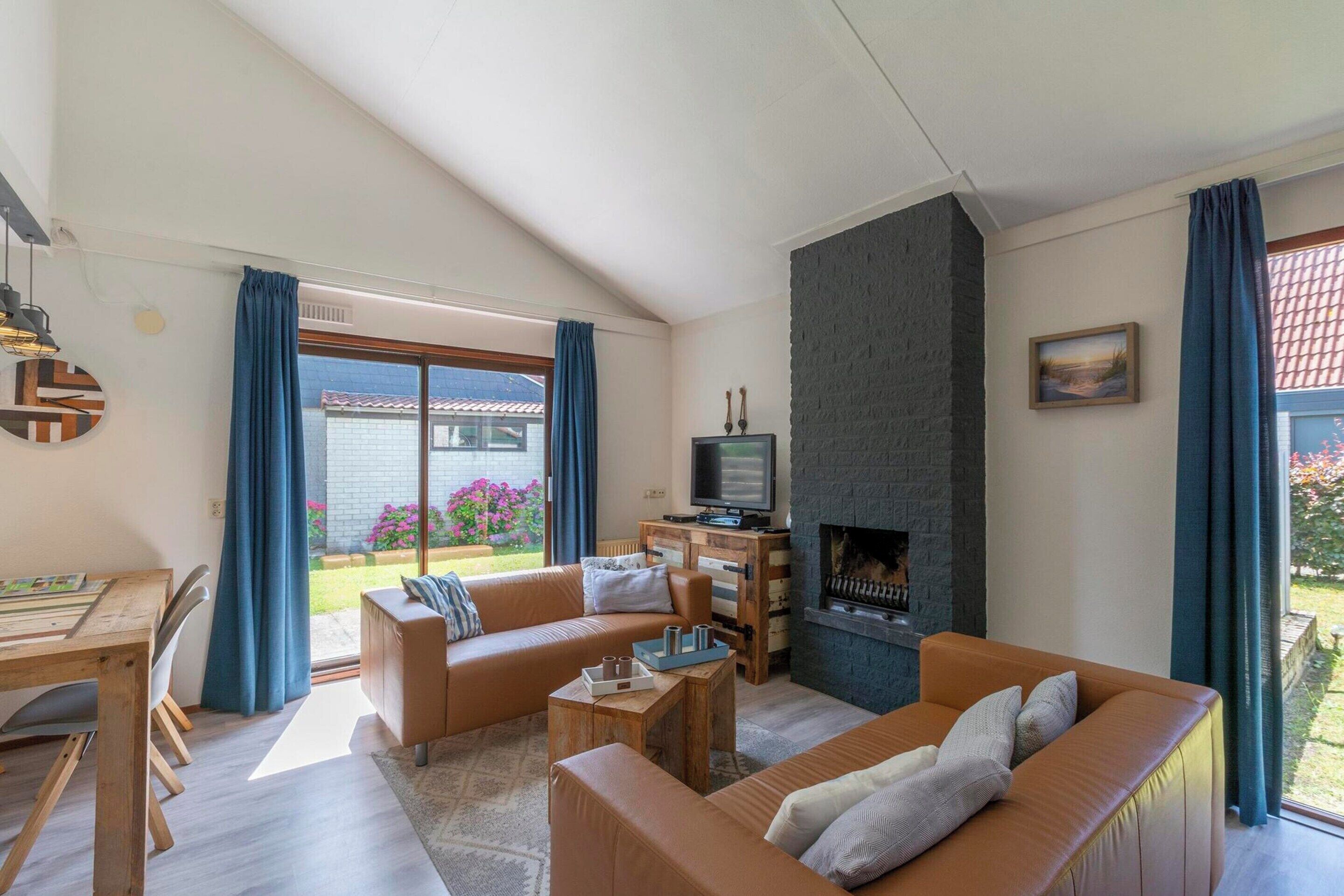 A modern living room with a fireplace, sofas, a TV, and a dining area with a table and chairs.