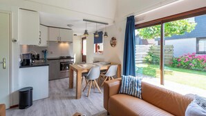 A compact living space with a kitchenette, dining area, and a large window offering a view of a garden. - Yperhof 66 Holiday Home for 6 Guests on Cost (Julianadorp)