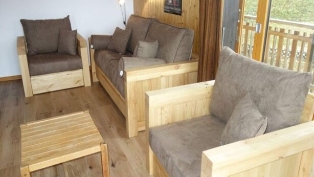 A room with three wooden sofas and a small wooden table, with a wooden wall and a poster on the wall. - Apartment in Valais Near Cable Car (Nendaz)