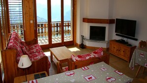 A cozy living room with a fireplace, a television, and a balcony with wooden railings. - Apartment in Valais Near Cable Car (Nendaz)