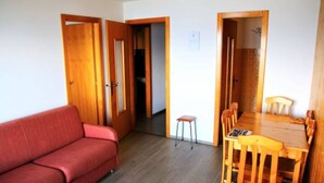 A compact living space with a red sofa, a wooden dining table with chairs, and a small stool. - Apartment in Valais Near Cable Car (Nendaz)