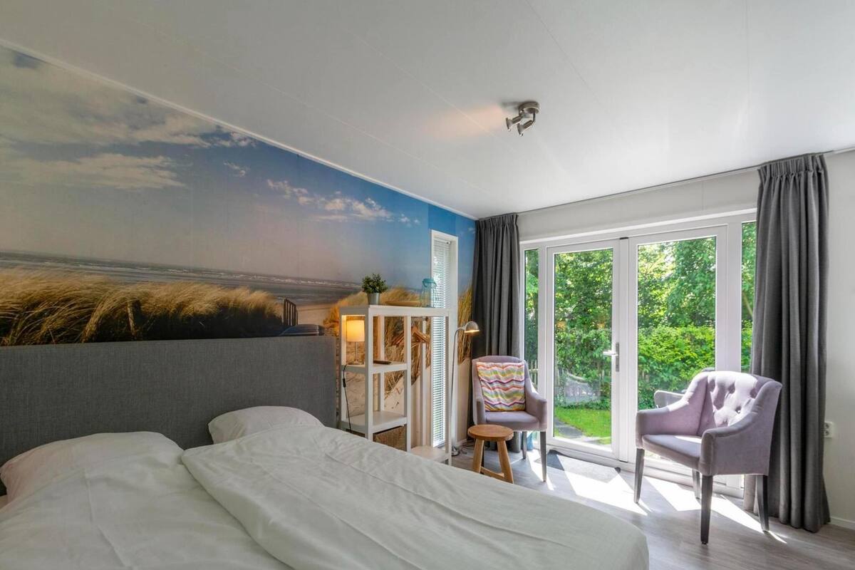 A bedroom with a large bed, a desk with a chair, and a view of the outdoors.