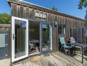 Un edificio de madera con un letrero que dice 'NOOR' y una puerta de vidrio que da acceso a un dormitorio con una cama y una silla.