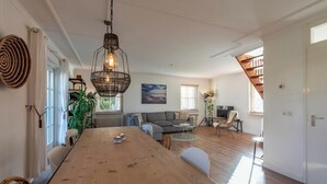 A spacious living area with a wooden dining table, a sofa, and a staircase. - Dutch Beach Hideaway w/ Parking (Callantsoog)