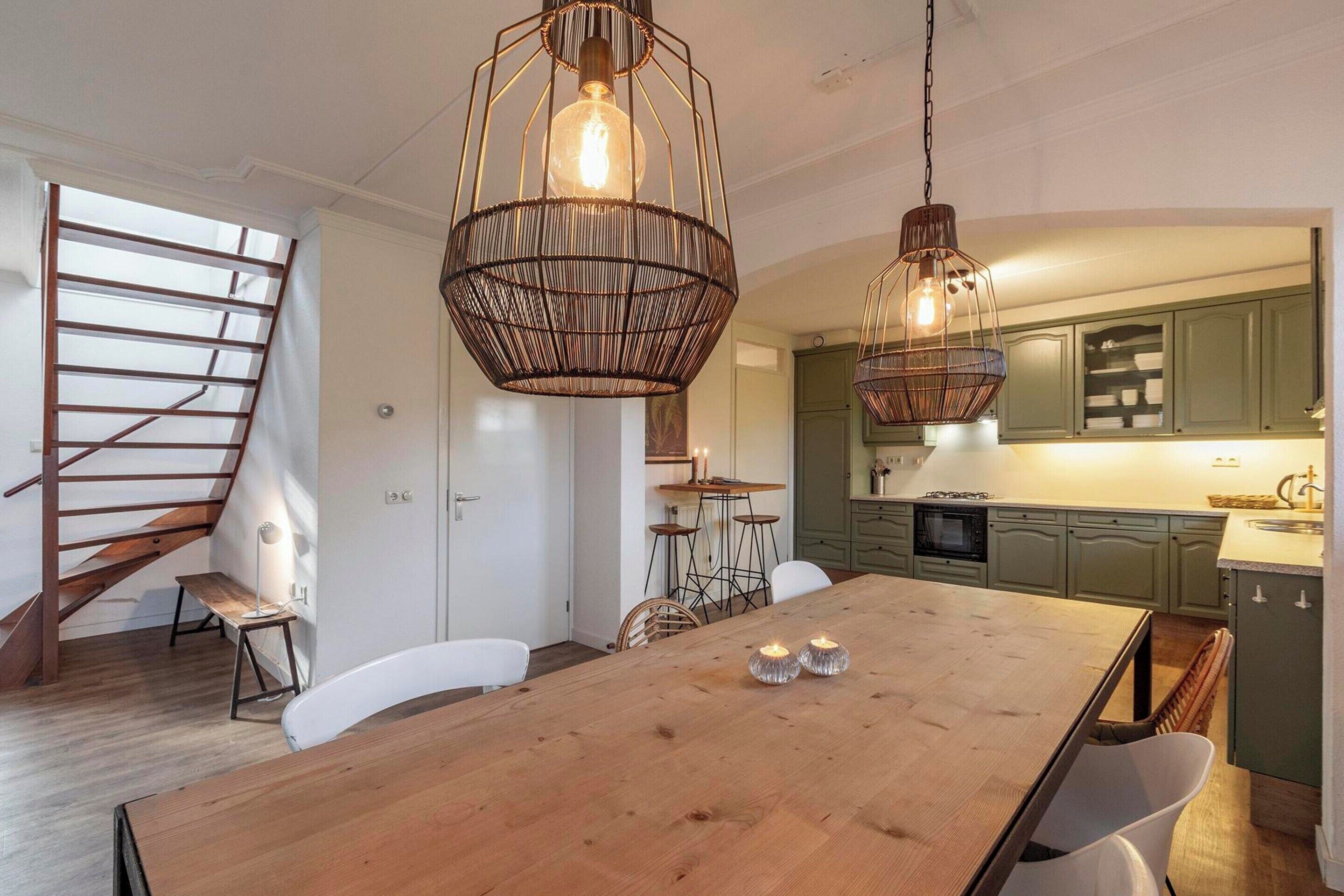 A modern kitchen with green cabinets, a wooden dining table with candles, and a staircase with a metal railing.