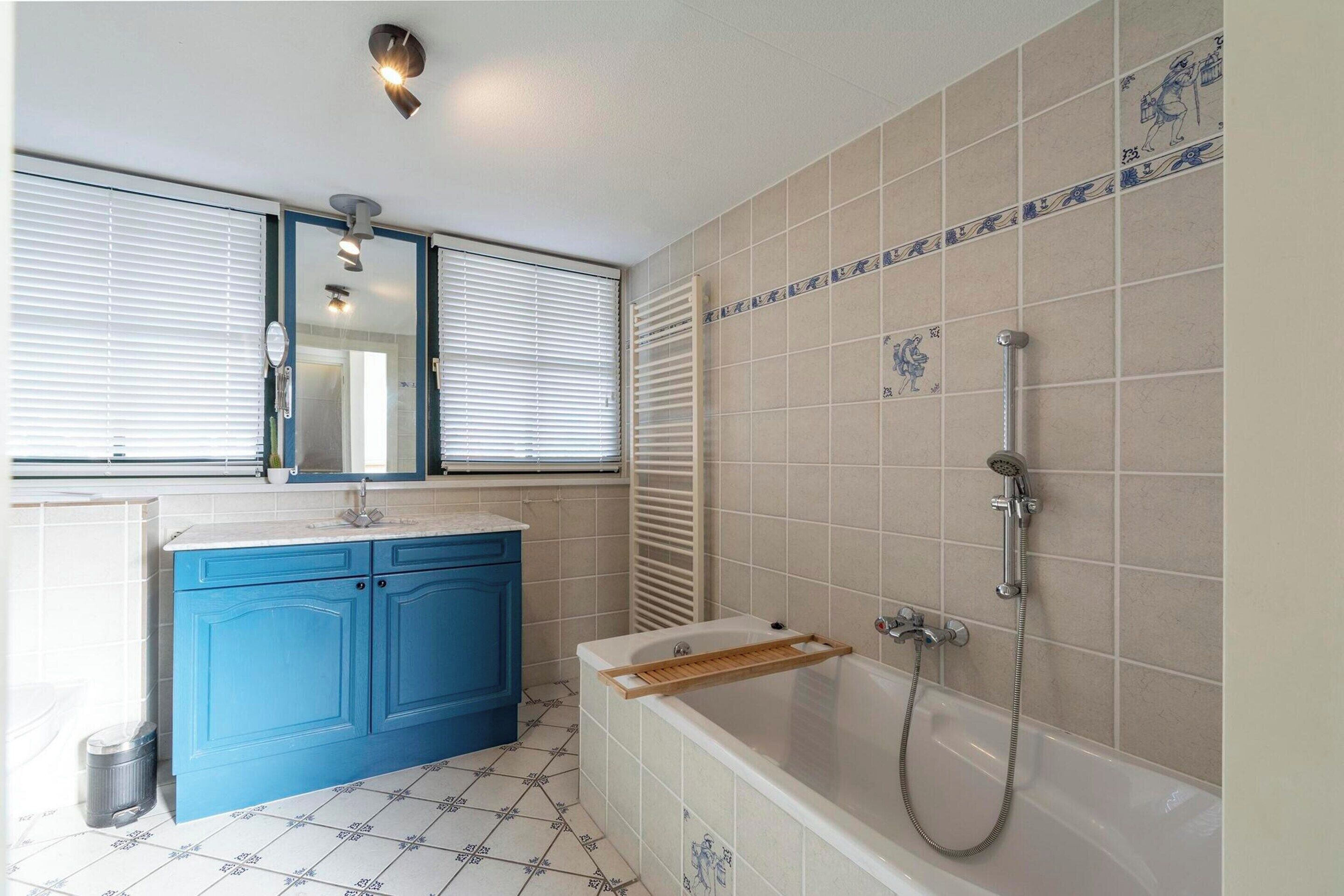 A bathroom with a bathtub, a vanity with a mirror, and tiled walls.