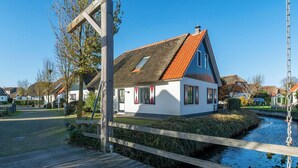 A house with a thatched roof, white walls, and a wooden dock extending over a canal. - Dutch Beach Hideaway w/ Parking (Callantsoog)