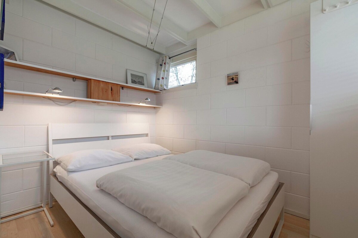 A bedroom with a single bed, white walls, and a window with a curtain.