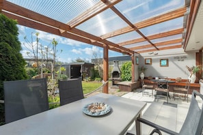 A covered patio with a table set for dining, a grill, and a garden view. - Wildrijk 152 Holiday Home in Sint Maartenszee (Sint Maartensvlotbrug)