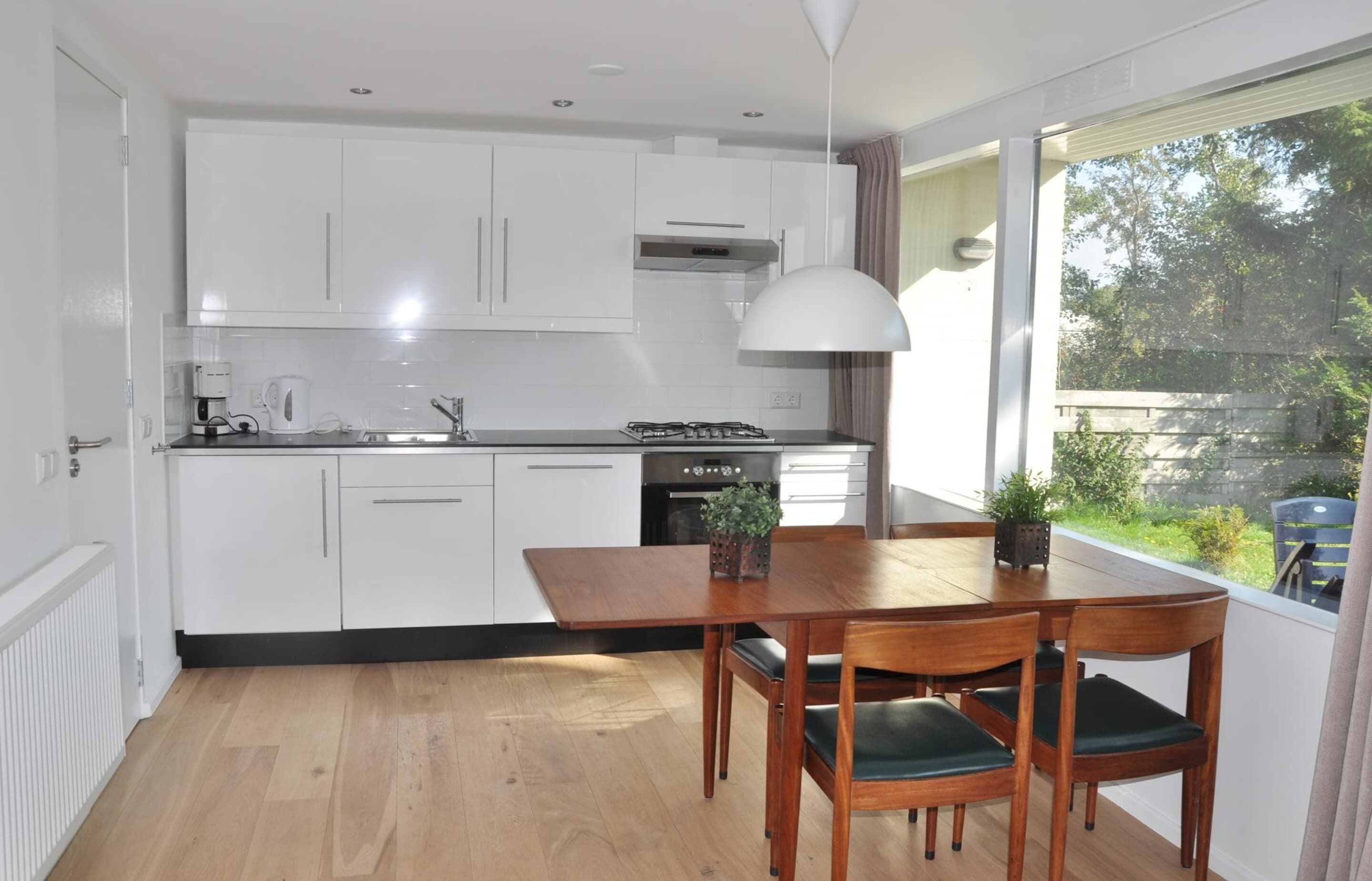 Una cocina moderna con armarios blancos, una mesa de comedor con sillas y vistas al exterior.