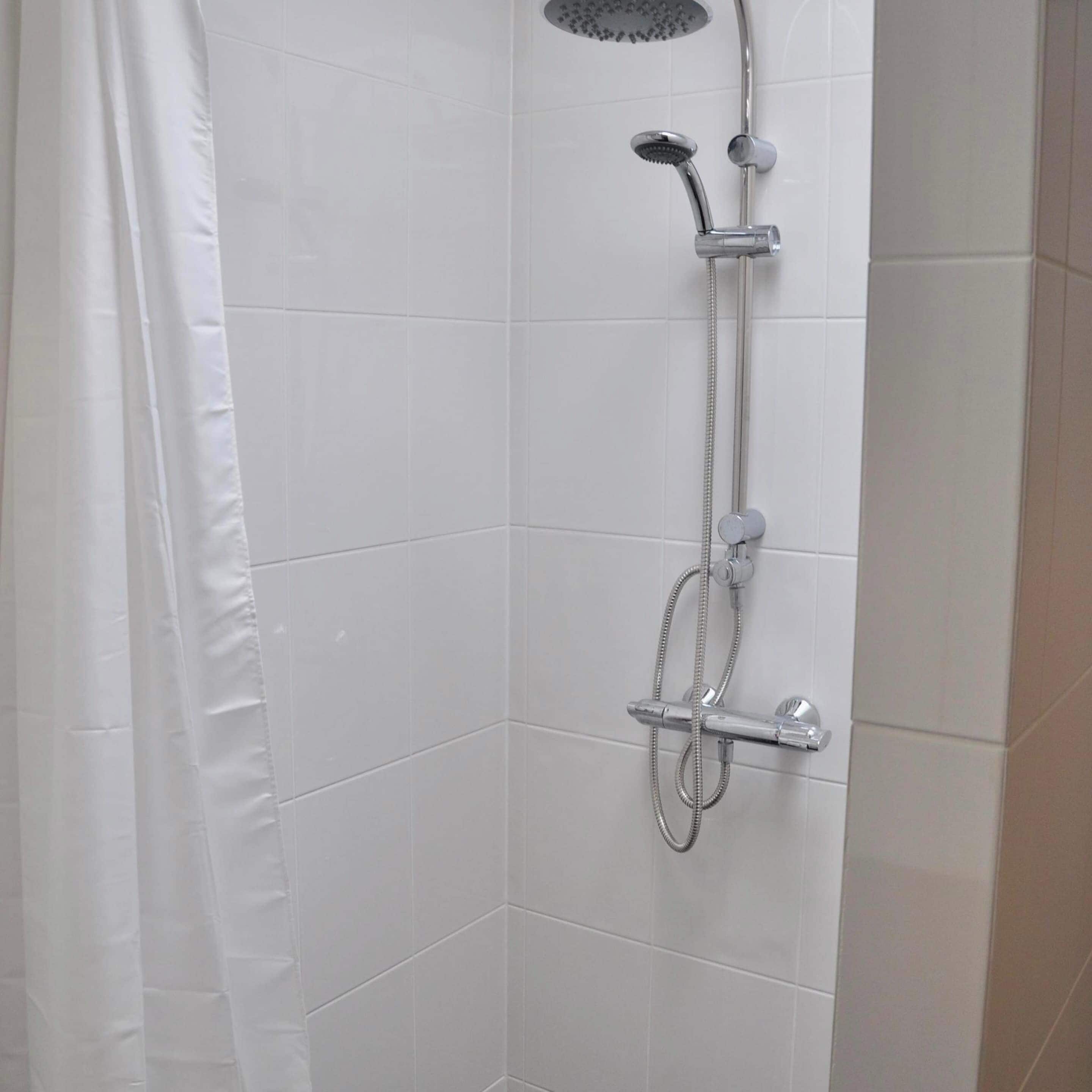 A shower with a handheld showerhead, a wall-mounted faucet, and a handheld showerhead.