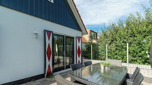 A patio with a glass-top table and wicker chairs, a sliding glass door, and a brick wall. - Villa in Callantsoog Near the Beach (Callantsoog)
