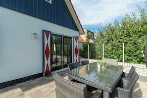 A patio with a glass-top table and wicker chairs, a sliding glass door, and a brick wall. - Villa in Callantsoog Near the Beach (Callantsoog)