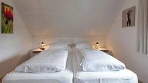 A twin room with two beds, bedside tables, lamps, and artwork on the walls. - Villa in Callantsoog Near the Beach (Callantsoog)