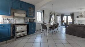 A kitchen with blue cabinets, a dining table with chairs, a white stove, and a chandelier. - Villa in Callantsoog Near the Beach (Callantsoog)