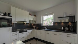A modern kitchen with white cabinets, a black countertop, and a window with a view of greenery. - Villa in Callantsoog Near the Beach (Callantsoog)