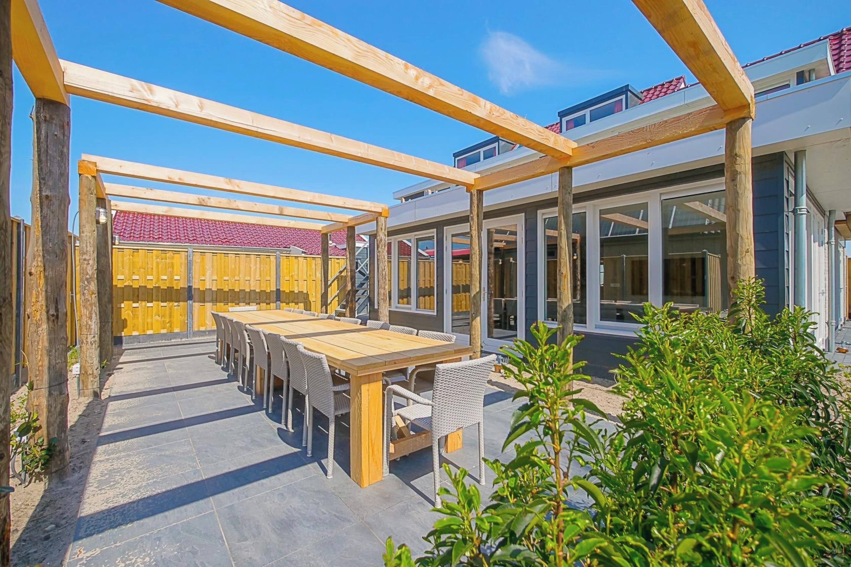 A covered patio area with a wooden table and chairs, surrounded by a wooden pergola.