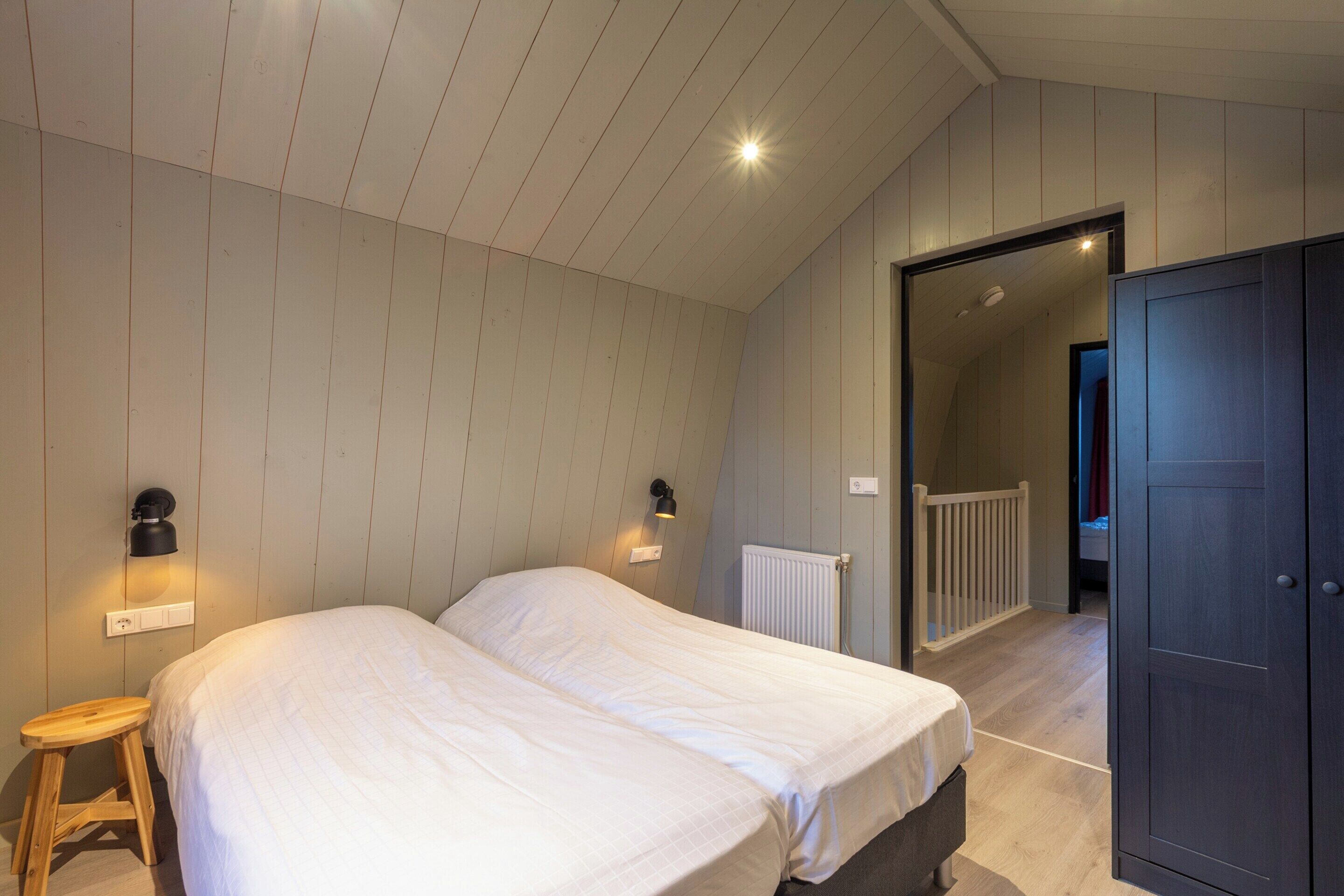Quarto com duas camas, soalho de madeira, radiador e um guarda-roupa.