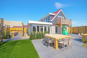 A modern house with a large patio, outdoor furniture, and a wooden deck. - Callantsoog Group Getaway Beach (Callantsoog)