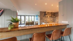 A modern kitchen with a wooden bar, four bar stools, and a large window. - Callantsoog Group Getaway Beach (Callantsoog)