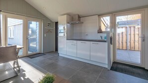 A modern kitchen with white cabinets, a black countertop, and a stainless steel range hood. There is a sliding glass door leading to a patio area. - Callantsoog Group Getaway Beach (Callantsoog)