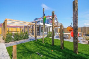 A modern building with a red-tiled roof, a wooden pergola, and a flagpole with a flag. - Callantsoog Group Getaway Beach (Callantsoog)
