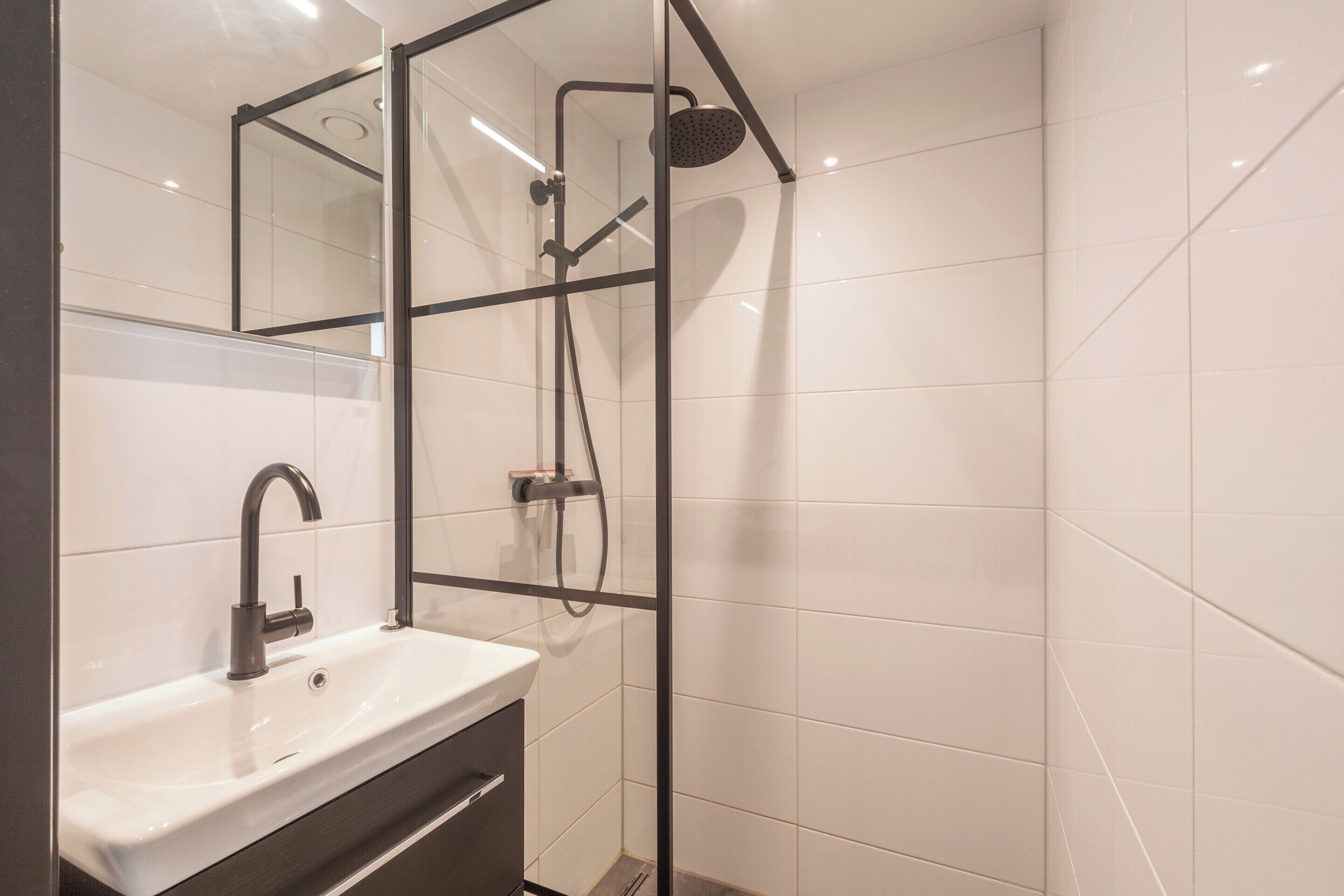A modern bathroom with a glass shower enclosure, a white sink, and a mirror.
