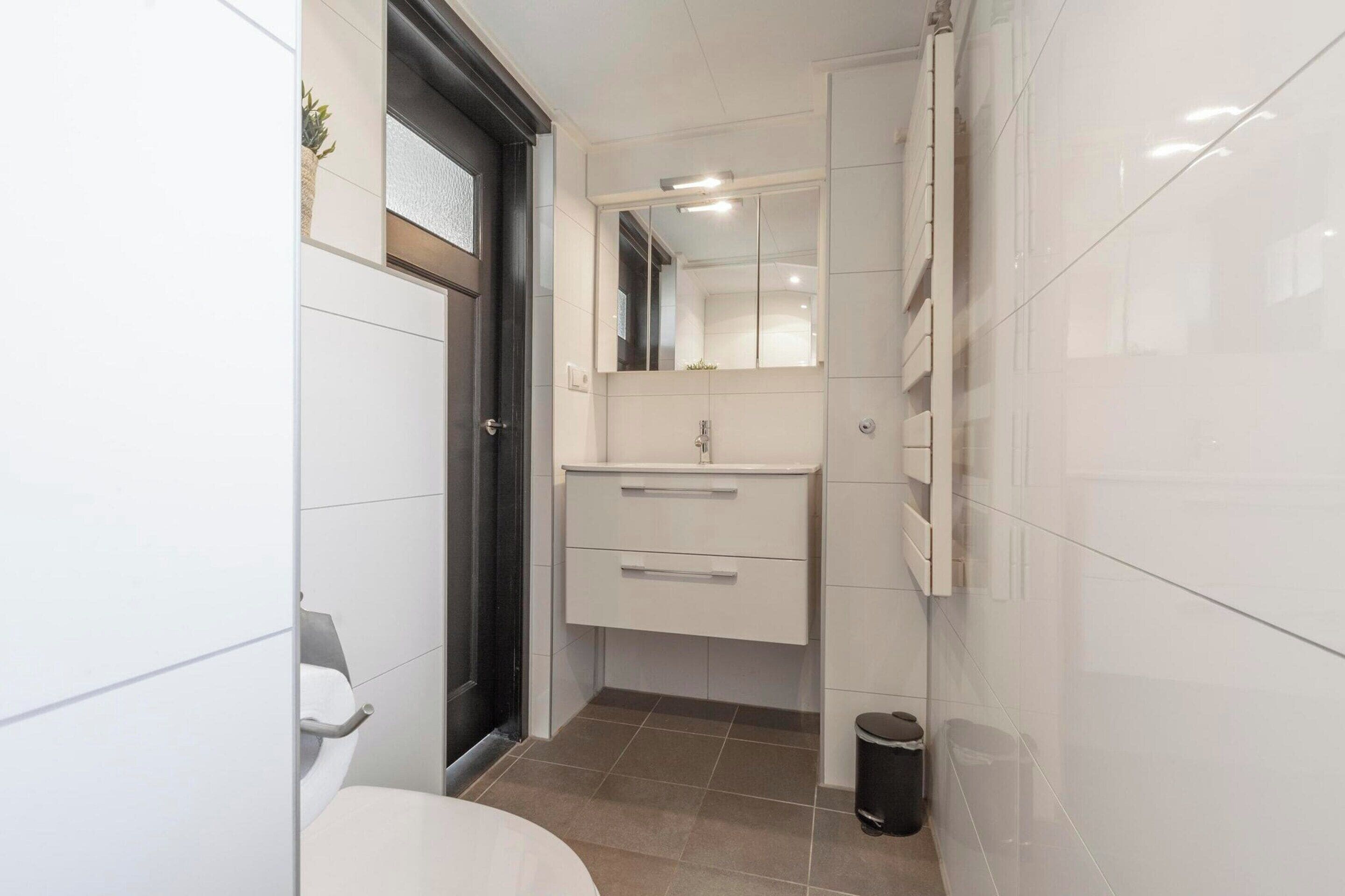 Une petite salle de bain comprenant des toilettes, un lavabo avec un miroir et une poubelle.