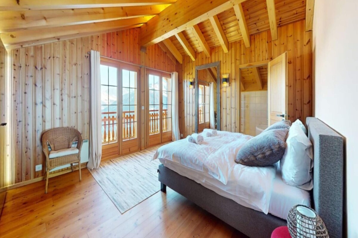 Ein Schlafzimmer in einer Holzhütte mit einem Bett, einem Sessel und einem Balkon.