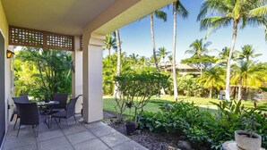 Une terrasse couverte avec des sièges d’extérieur, entourée d’une végétation luxuriante et de palmiers.