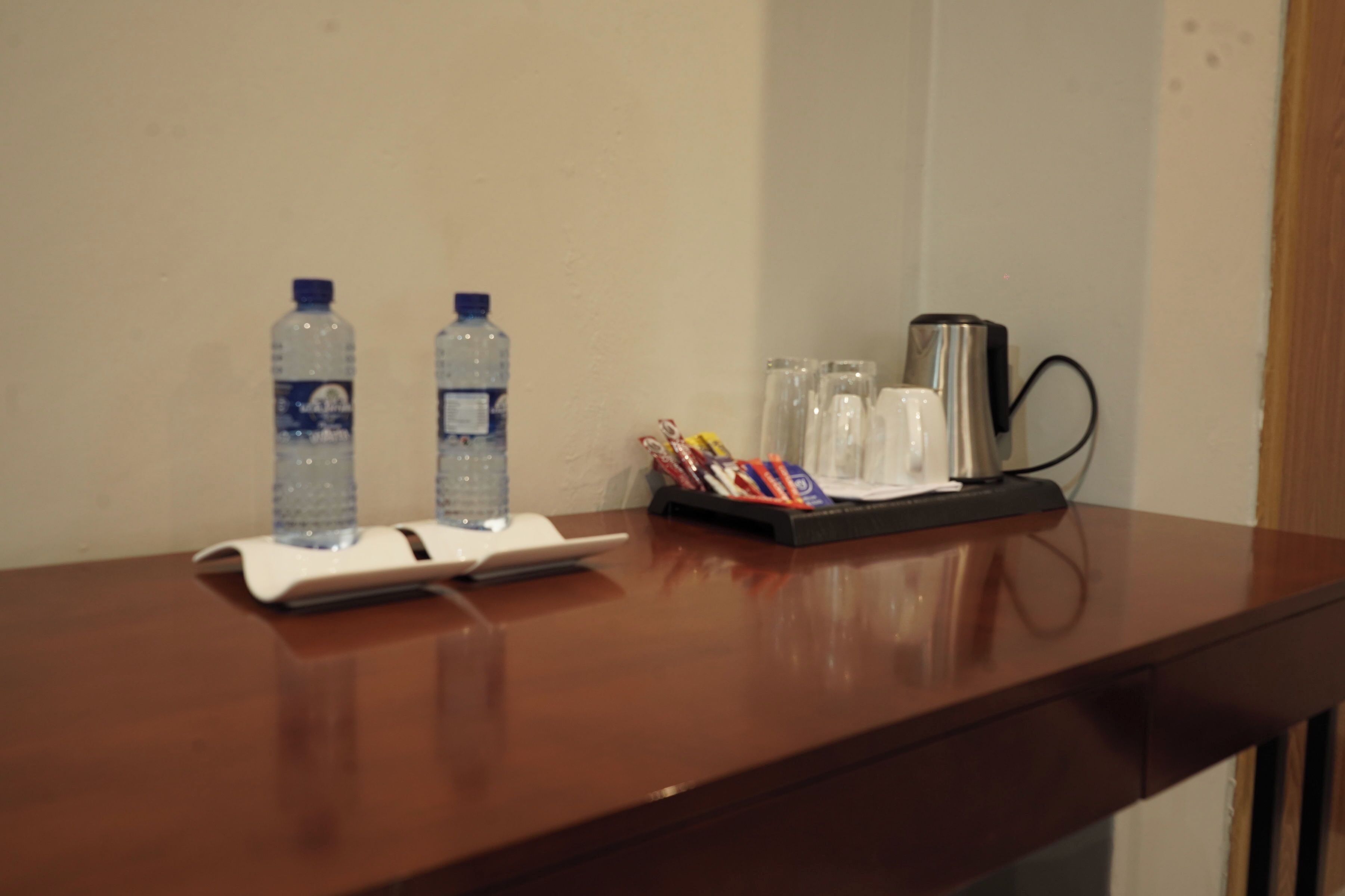 A wooden table with two water bottles, a coffee maker, and a pen holder with pens.