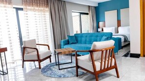 Ein modernes Hotelzimmer mit einem blauen Sofa, zwei Sesseln, einem kleinen Holztisch und einem Bett mit weißer Bettwäsche.