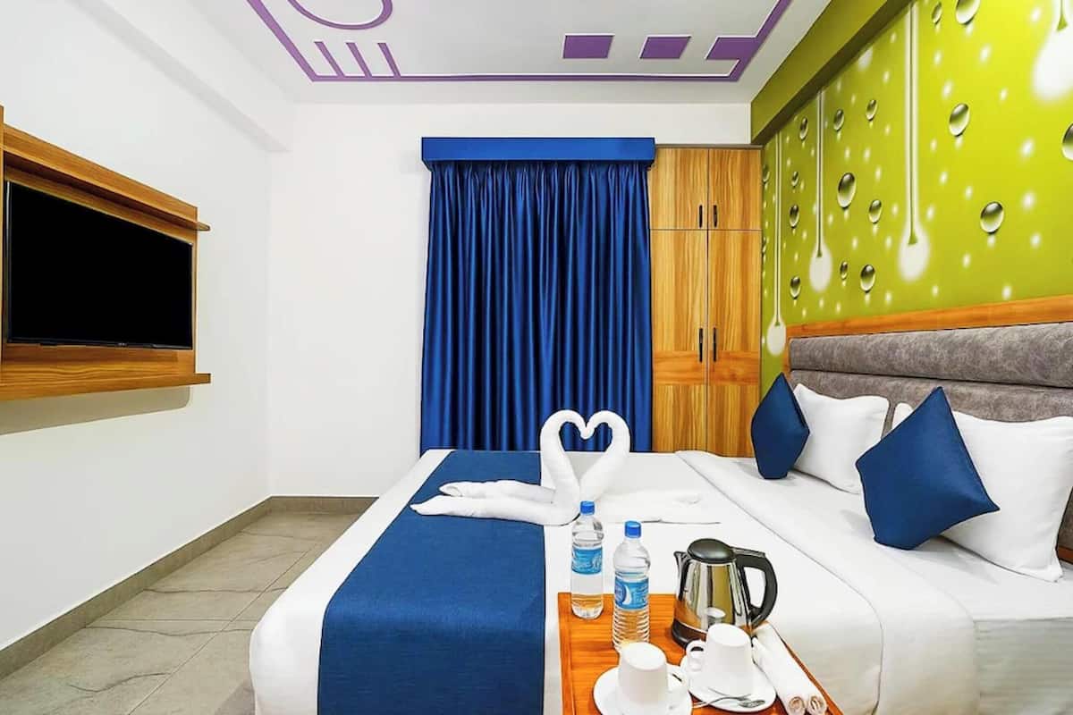 Habitación de hotel con cama, televisor, mueble de madera, pared verde con diseño de gotas de agua y cortina azul.