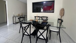 A dining area with a glass table, black chairs, a window, and a red cabinet in the background. - EDS Hébergement meublé (Abidjan)